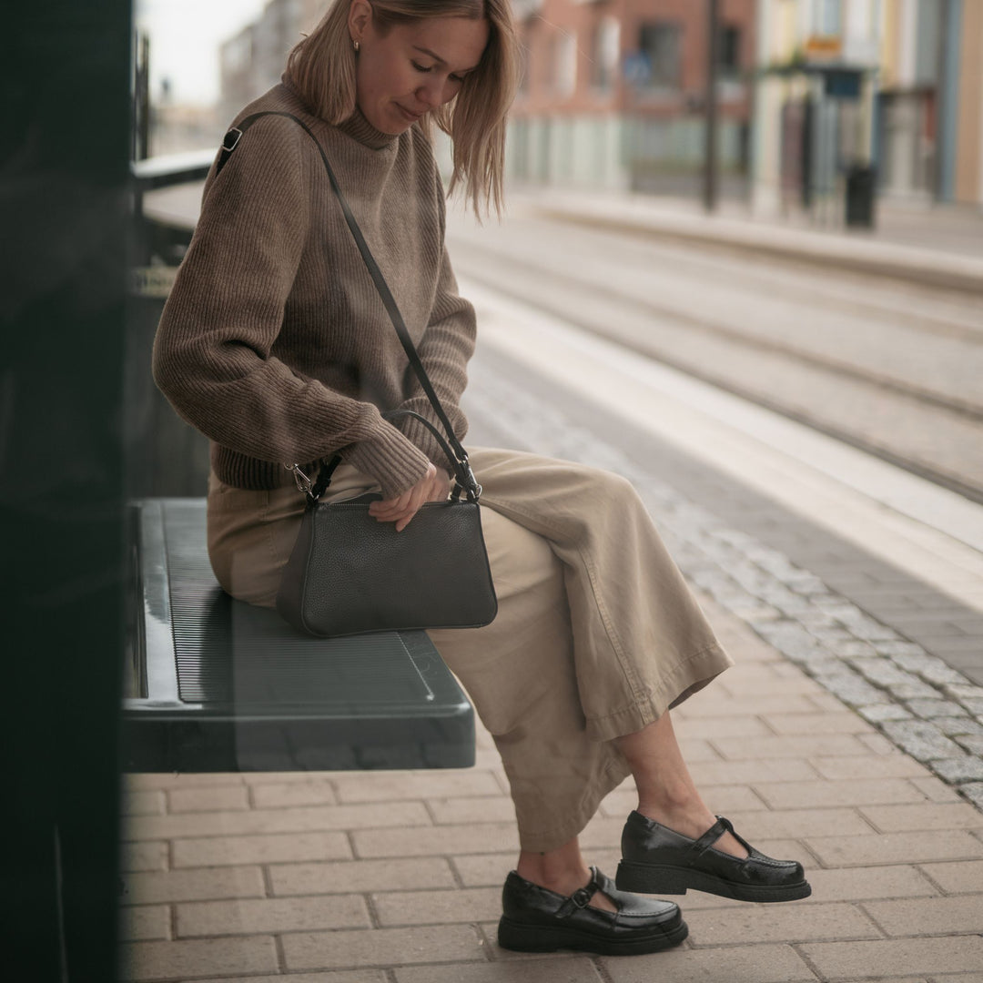 Person wearing mary jane shoes sitting at the bus stop and looking into their bag.