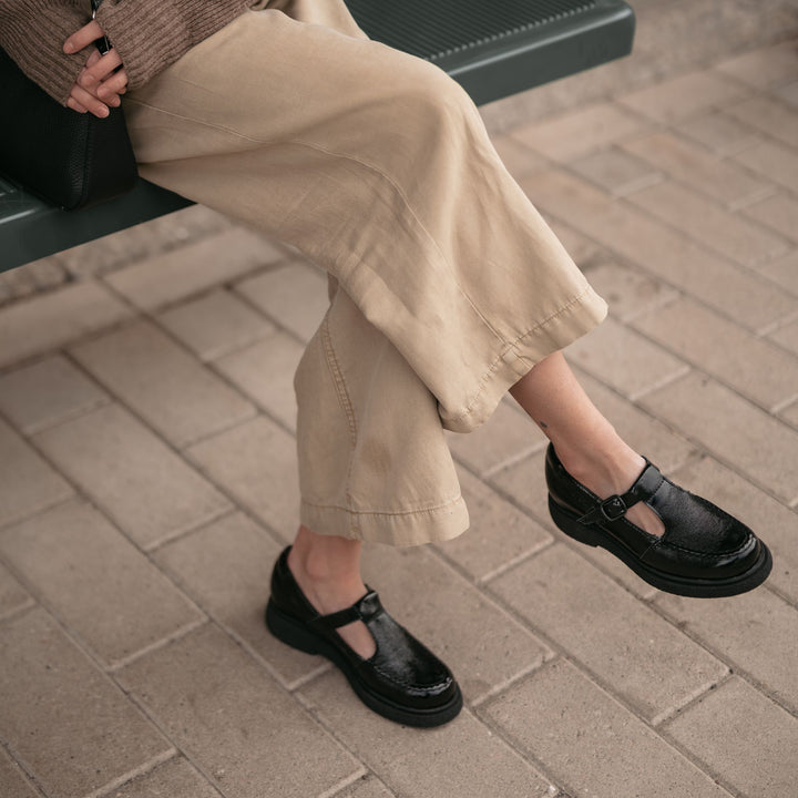 Close-up image of a person sitting on a bench wearing mary jane shoes.